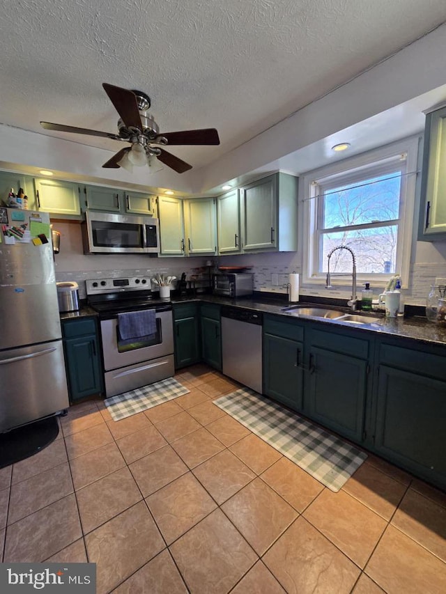 kitchen with light tile patterned floors, stainless steel appliances, a sink, dark countertops, and green cabinetry