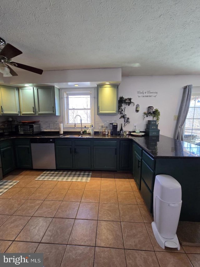 kitchen featuring dishwasher, a peninsula, dark countertops, and a sink