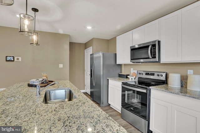 kitchen featuring appliances with stainless steel finishes, white cabinets, a sink, and decorative light fixtures