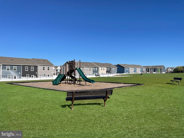 communal playground featuring a lawn, fence, and a residential view