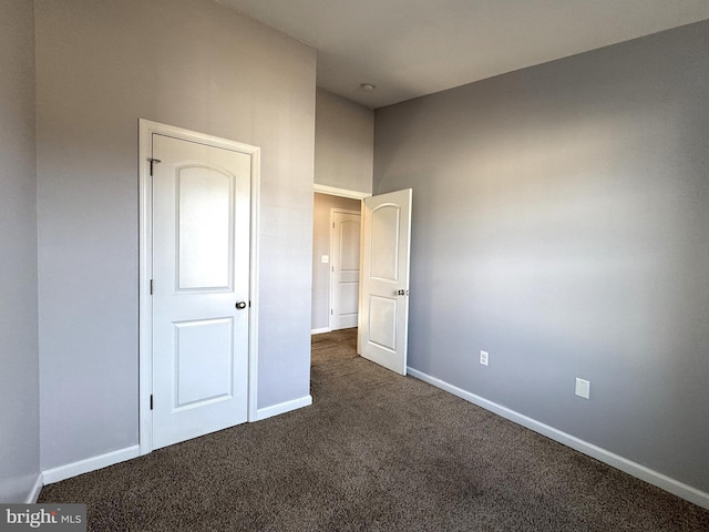 unfurnished bedroom with dark carpet and baseboards