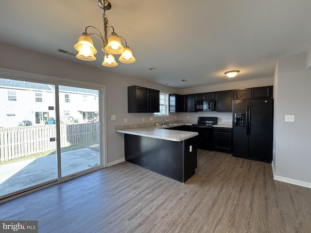 kitchen with decorative light fixtures, light countertops, wood finished floors, a peninsula, and black appliances