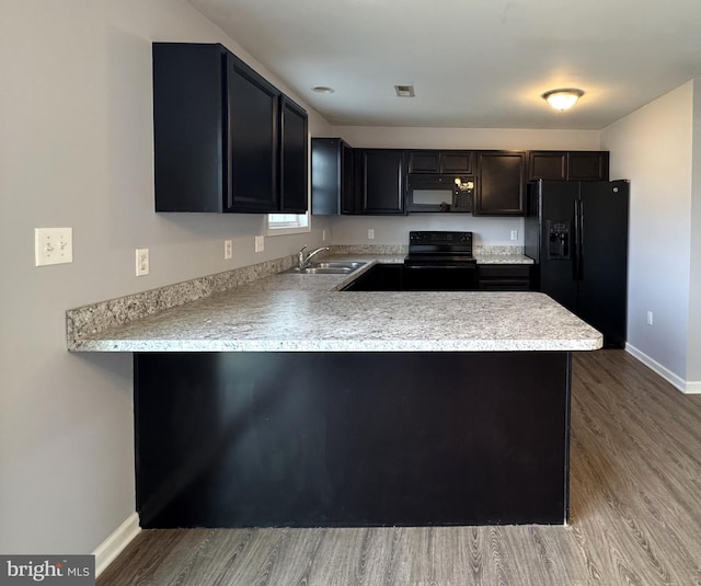 kitchen featuring a peninsula, black appliances, light countertops, and a sink