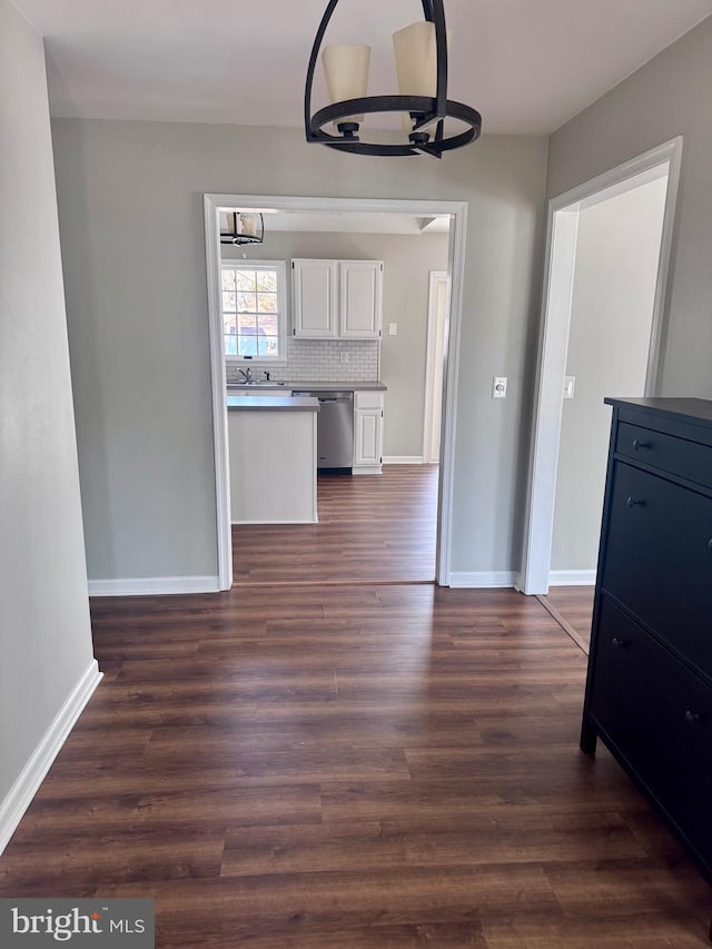 unfurnished dining area featuring baseboards, an inviting chandelier, and dark wood finished floors