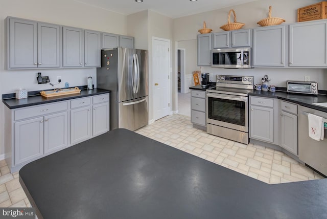 kitchen with appliances with stainless steel finishes, dark countertops, gray cabinets, and a toaster