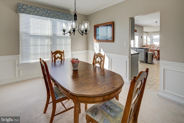 dining room featuring light carpet, ornamental molding, a wainscoted wall, and an inviting chandelier