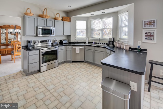 kitchen with appliances with stainless steel finishes, dark countertops, a sink, and gray cabinetry