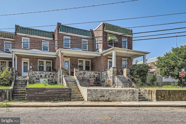 townhome / multi-family property featuring covered porch, stairs, and brick siding