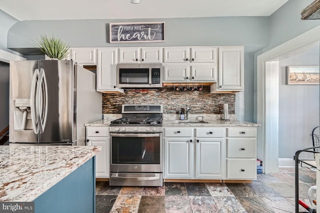 kitchen with a sink, white cabinets, appliances with stainless steel finishes, decorative backsplash, and stone tile flooring