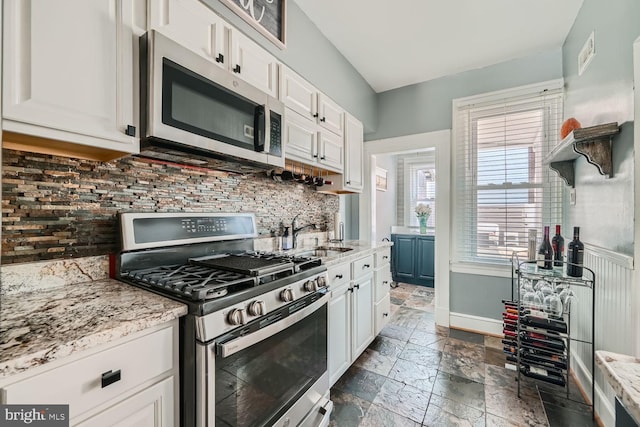 kitchen with appliances with stainless steel finishes, stone tile flooring, white cabinetry, and a sink