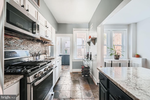 kitchen with light stone countertops, white cabinetry, stainless steel appliances, and stone tile flooring