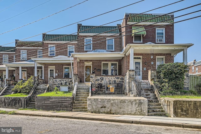 multi unit property with covered porch, brick siding, and stairway