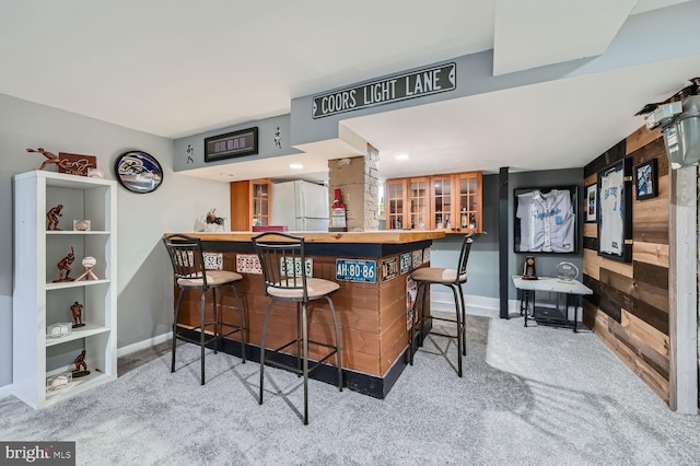 bar with light carpet, bar area, freestanding refrigerator, and baseboards