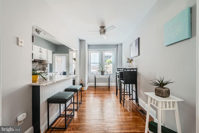 kitchen with a breakfast bar, dark wood-style flooring, white cabinetry, baseboards, and backsplash