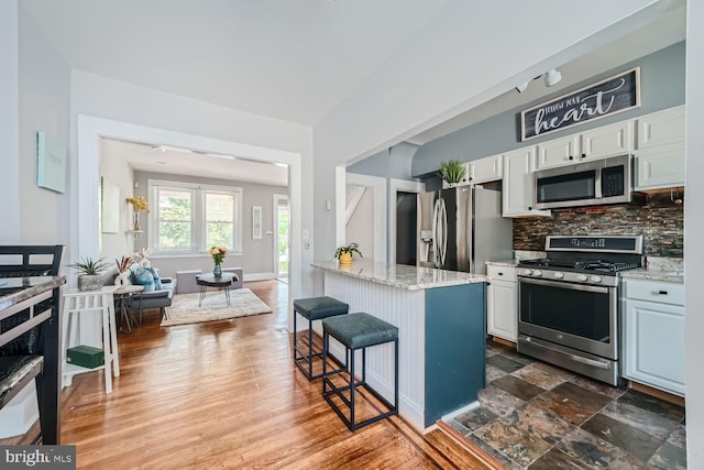 kitchen with light stone counters, stainless steel appliances, a breakfast bar, white cabinets, and decorative backsplash