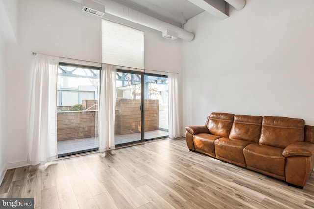 living area with light wood-style floors, beam ceiling, and a towering ceiling