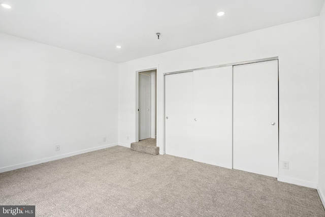 unfurnished bedroom with light carpet, a closet, baseboards, and recessed lighting