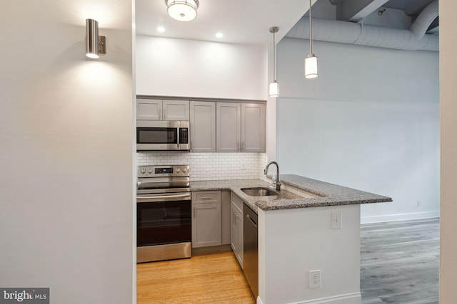 kitchen with dark stone counters, appliances with stainless steel finishes, a peninsula, pendant lighting, and a sink