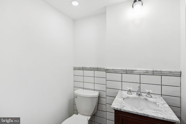 half bath featuring toilet, vanity, and tile walls