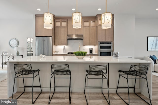 kitchen with under cabinet range hood, light wood-style floors, appliances with stainless steel finishes, and light countertops