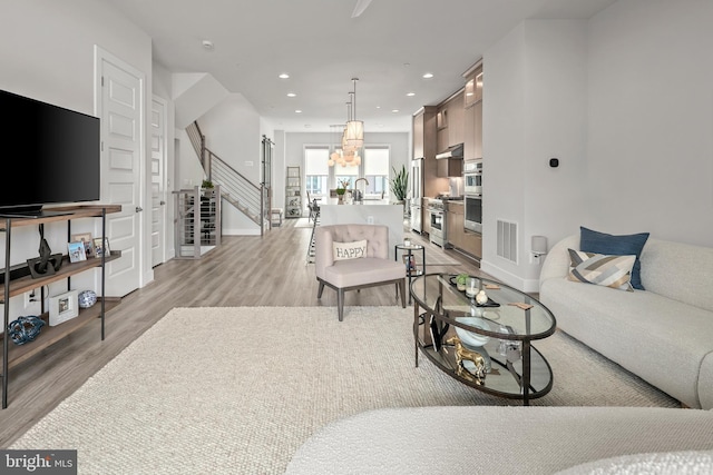 living room featuring light wood-type flooring, visible vents, a notable chandelier, recessed lighting, and stairs