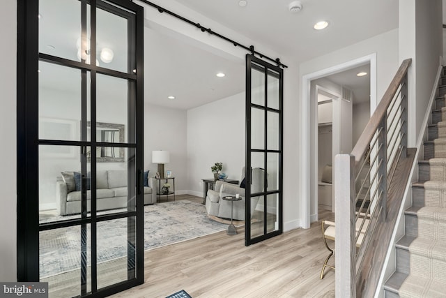 interior space featuring baseboards, stairs, light wood-type flooring, a barn door, and recessed lighting