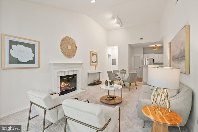 living room featuring track lighting, light carpet, a fireplace, high vaulted ceiling, and baseboards