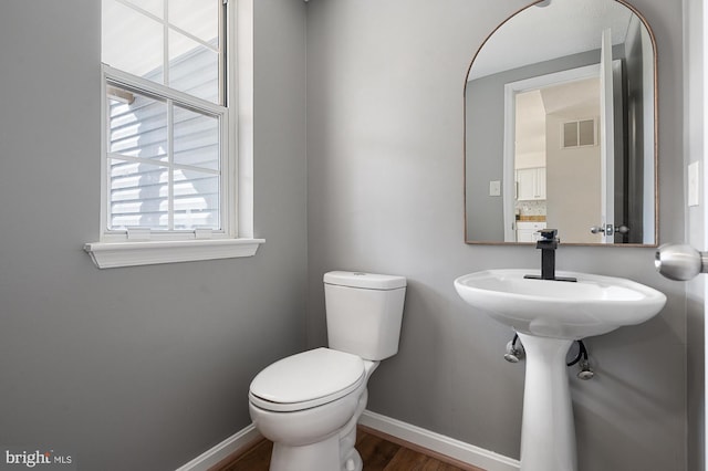 half bath featuring toilet, baseboards, visible vents, and wood finished floors