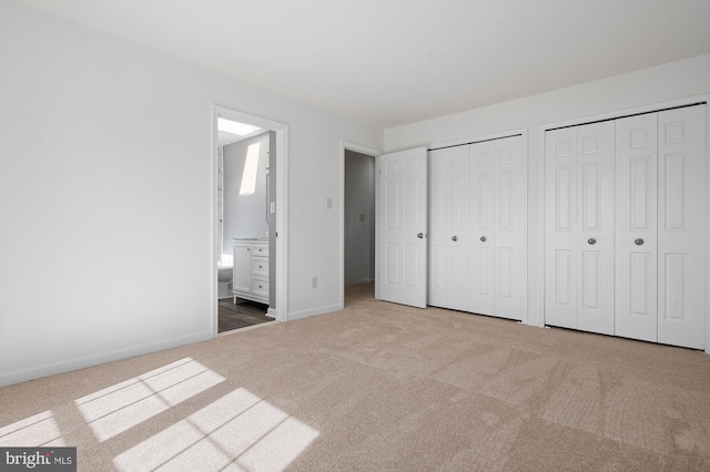 unfurnished bedroom featuring baseboards, carpet, ensuite bath, and multiple closets