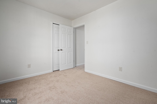 unfurnished bedroom featuring light carpet, baseboards, and a closet