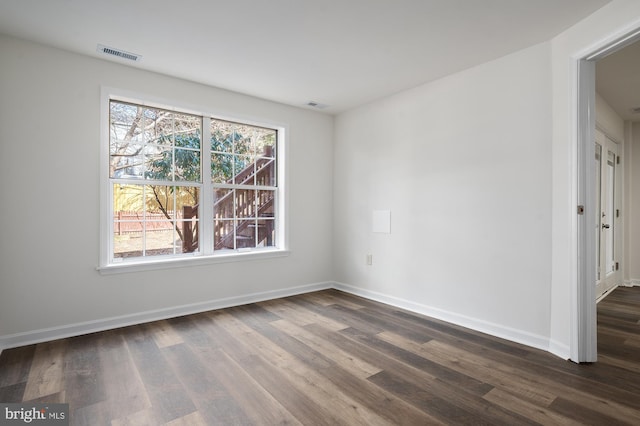 empty room with visible vents, dark wood finished floors, a wealth of natural light, and baseboards