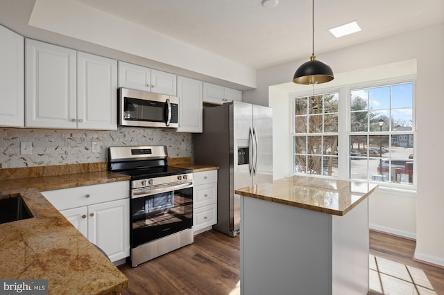 kitchen with appliances with stainless steel finishes, white cabinets, hanging light fixtures, and light stone counters