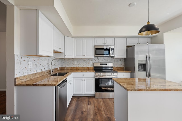 kitchen featuring appliances with stainless steel finishes, light stone countertops, white cabinetry, pendant lighting, and a sink