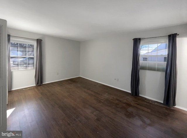 spare room featuring visible vents, baseboards, and dark wood finished floors