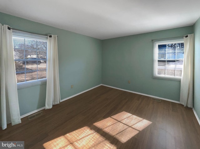 unfurnished room featuring plenty of natural light, visible vents, and dark wood finished floors