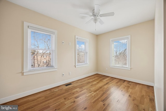 empty room featuring a ceiling fan, baseboards, visible vents, and wood finished floors