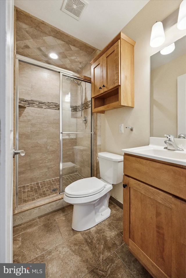 bathroom with toilet, vanity, visible vents, baseboards, and a shower stall