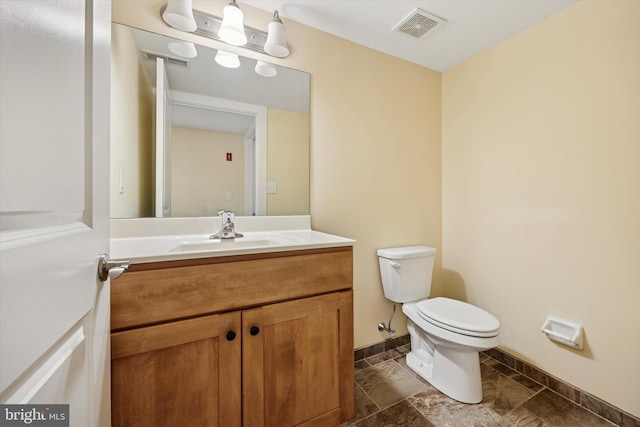 bathroom featuring visible vents, toilet, stone finish floor, vanity, and baseboards