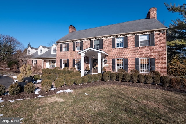 colonial inspired home featuring a chimney, a front lawn, and brick siding