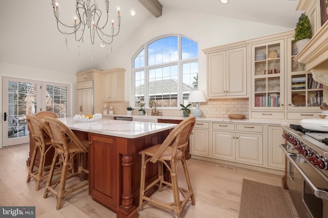 kitchen with range with two ovens, cream cabinetry, glass insert cabinets, a kitchen island, and a sink