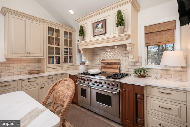 kitchen featuring lofted ceiling, a breakfast bar area, cream cabinetry, double oven range, and glass insert cabinets