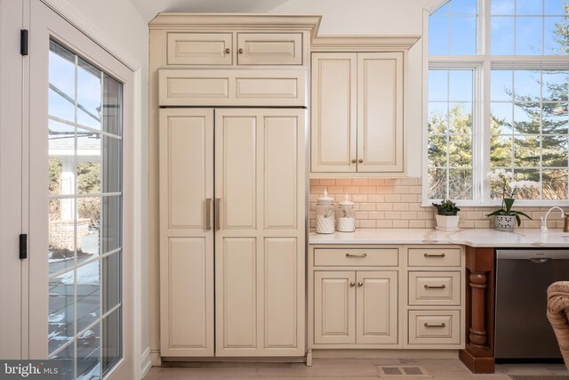 kitchen with visible vents, stainless steel dishwasher, cream cabinetry, backsplash, and light stone countertops