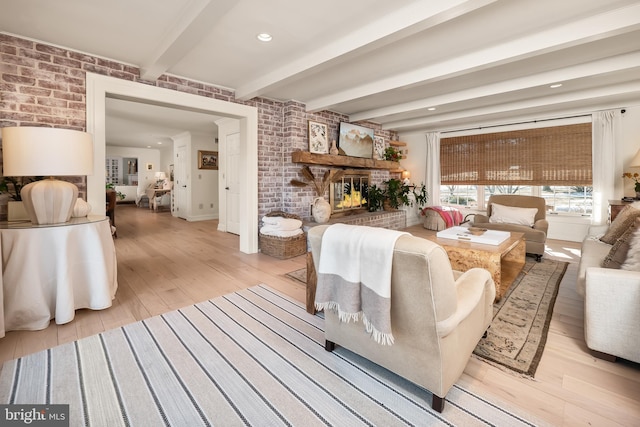 living room featuring beam ceiling, brick wall, a fireplace, and light wood finished floors