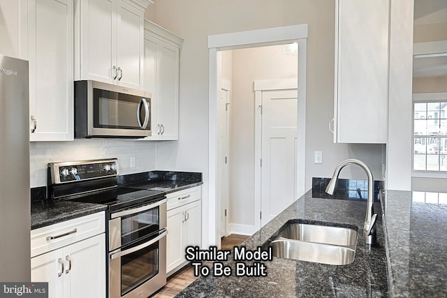 kitchen with dark stone counters, stainless steel appliances, a sink, and white cabinets