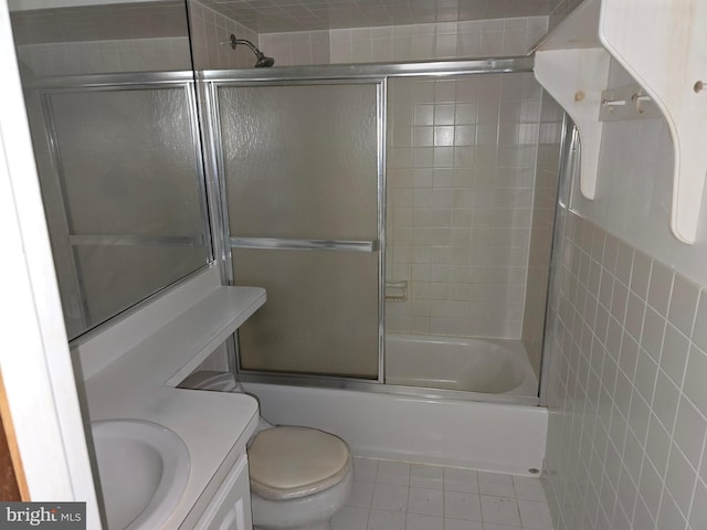 bathroom featuring toilet, tile patterned flooring, combined bath / shower with glass door, vanity, and tile walls