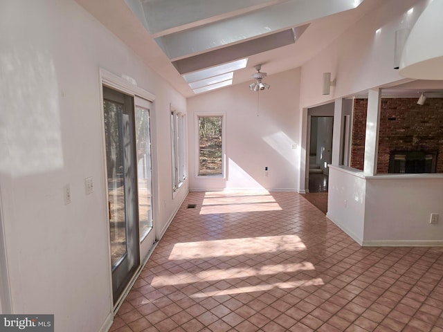 interior space featuring ceiling fan, light tile patterned floors, lofted ceiling with skylight, and baseboards