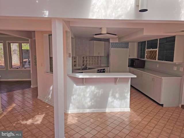 kitchen featuring a breakfast bar area, light countertops, white cabinets, a sink, and a peninsula