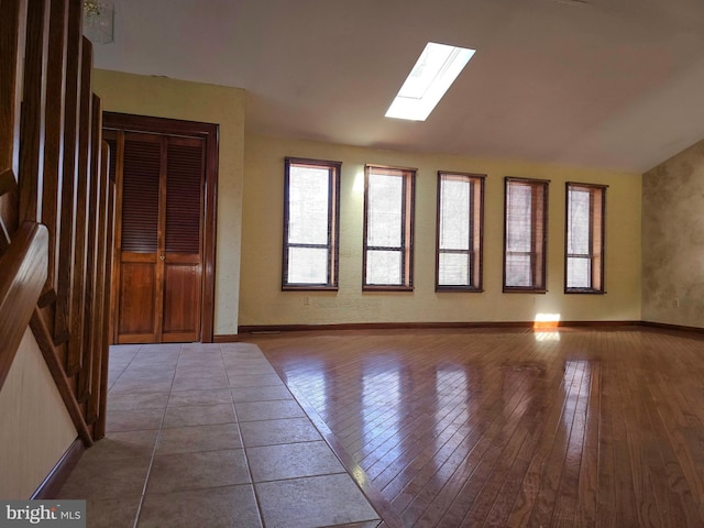 empty room featuring lofted ceiling with skylight, hardwood / wood-style flooring, and baseboards