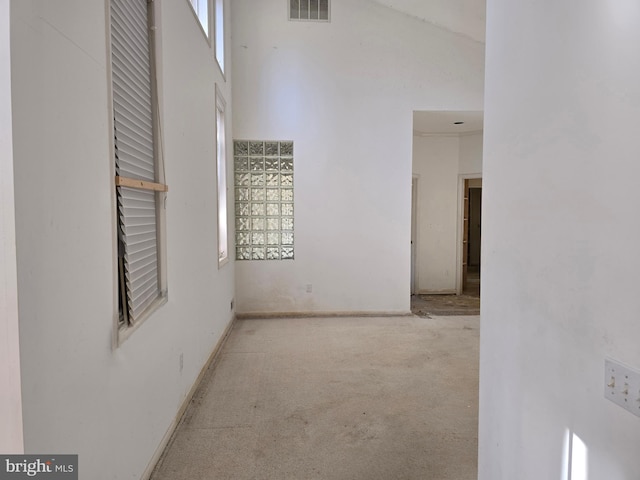 hall with a towering ceiling, baseboards, visible vents, and light colored carpet