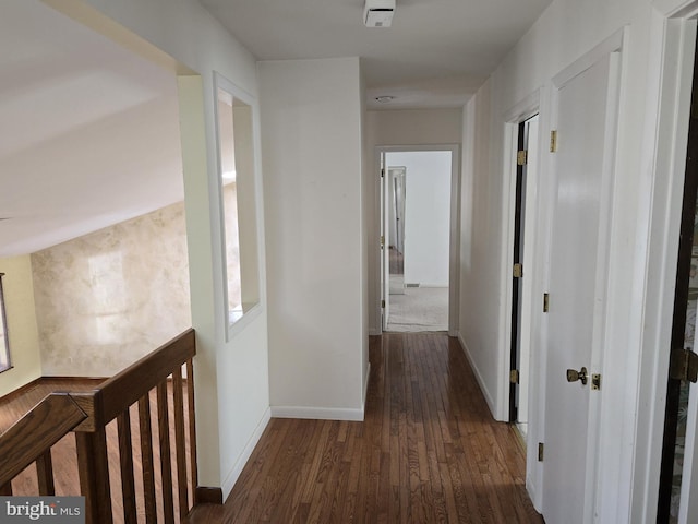 corridor with dark wood finished floors, an upstairs landing, and baseboards